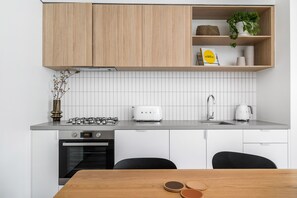 A modern kitchen with white cabinetry, a gas stove, a toaster, and a sink. - Axel Apartments 103 The Hadley (Glen Iris)