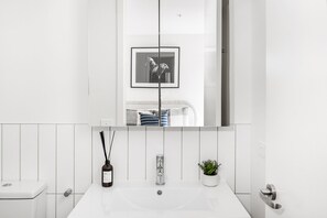 A modern bathroom with a large mirror, a sink, a toilet, and a framed picture on the wall. - Axel Apartments 103 The Hadley (Glen Iris)