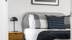 Ein Schlafzimmer mit Bett, Kissen, Nachttisch, Lampe und einem gerahmten Bild an der Wand.