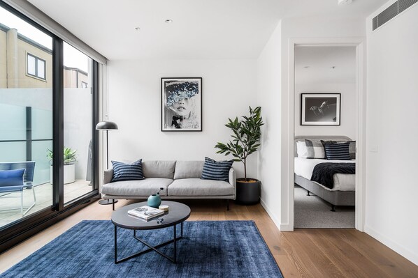 A modern living room with a sofa, a coffee table, and a potted plant. - Axel Apartments 103 The Hadley (Glen Iris)