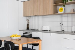 A modern kitchen with white cabinetry, a gas stove, a toaster, and a bowl of lemons on the counter. - Axel Apartments 103 The Hadley (Glen Iris)