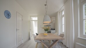 Un espace repas moderne avec une table en bois, des chaises blanches, un luminaire suspendu et une horloge au mur.