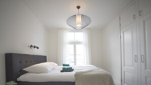 Une chambre moderne avec un grand lit, une table de chevet agrémentée d’une plante, un luminaire suspendu et une armoire.