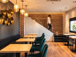 A modern interior with wooden tables and green chairs, a brick wall, and a staircase. - &Tales Suites - Óbidos (Obidos)