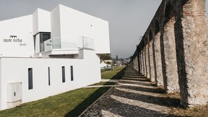 A modern building with a white facade, a glass balcony, and a stone wall adjacent to it. - &Tales Suites - Óbidos (Obidos)