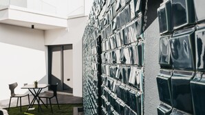 A modern building with a reflective facade, a patio area with outdoor seating, and a door leading to the interior. - &Tales Suites - Óbidos (Obidos)