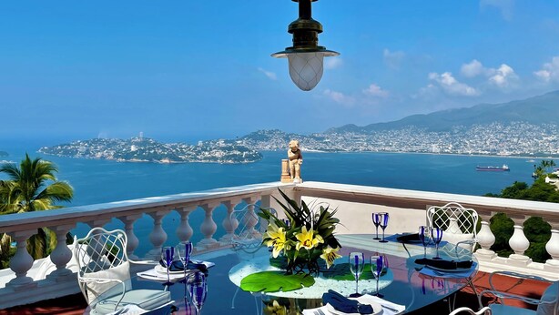 Une table dressée pour le dîner, avec vue sur une ville côtière et l’océan.