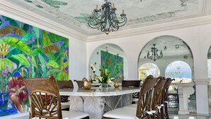 Un coin repas avec une table ronde, des chaises en osier et une fresque représentant un paysage tropical.