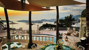 Une terrasse avec une table en verre, dressée pour le dîner, d’où l’on peut admirer un plan d’eau et des collines lointaines.