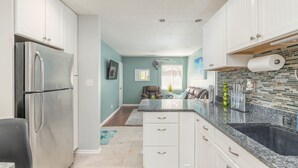 Una cocina moderna con armarios blancos, un refrigerador de acero inoxidable, encimera de granito y pileta negra.