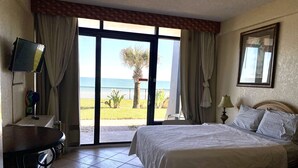 Een hotelkamer met een bed, een bureau, een televisie en uitzicht op het strand.