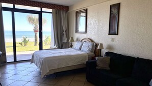 Een slaapkamer met een bed, een donkere bank, een raam met gordijnen en uitzicht op de oceaan.