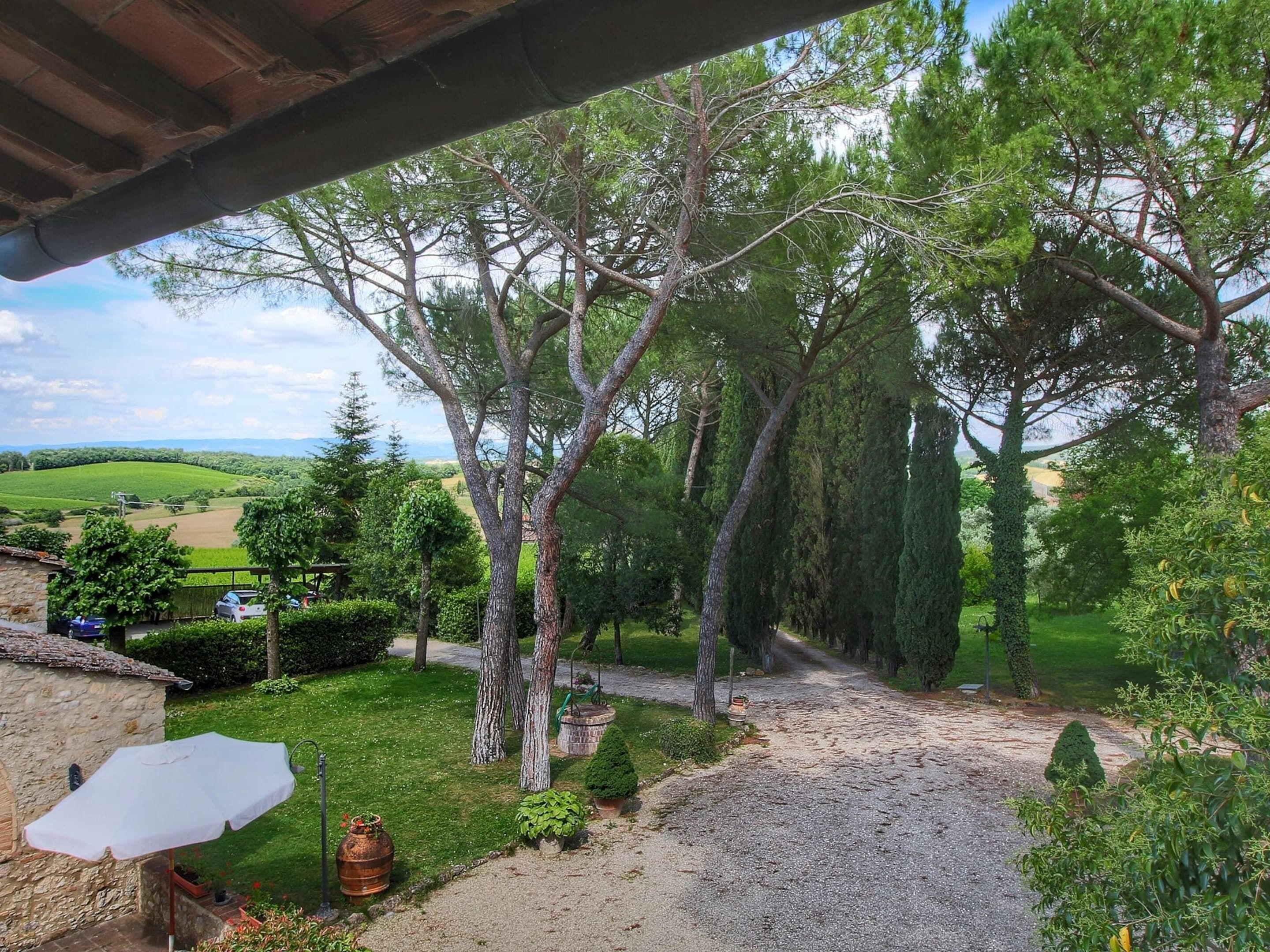 Un'area esterna coperta con un vialetto in ghiaia, alberi e vista su un paesaggio verde.