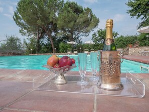 Escena junto a la piscina con una botella de champán, un cuenco de fruta y copas sobre una bandeja transparente.