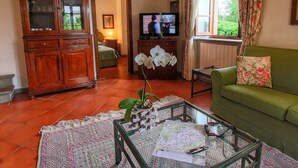 A living room with a green sofa, a wooden cabinet, a television, and a glass coffee table with a map and papers. - Holiday Home for 8 Guests (Siena)