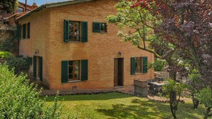 A two-story house with green shutters, a brick exterior, and a small garden area with a table and chairs. - Holiday Home for 8 Guests (Siena)