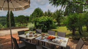 An outdoor dining area with wicker chairs and a table set with plates of food, cups, and a large umbrella. - Holiday Home for 8 Guests (Siena)