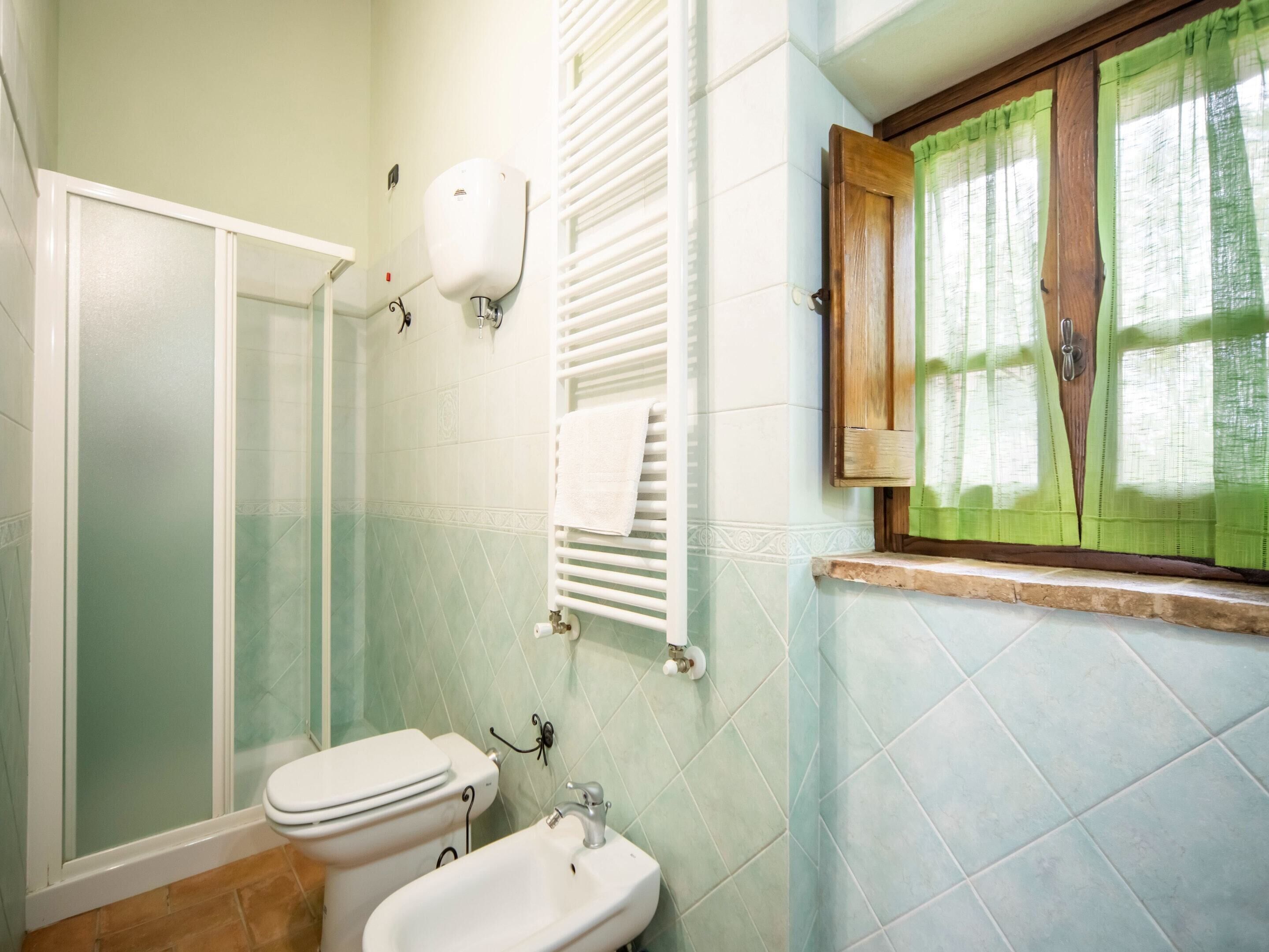 A bathroom with a shower, toilet, bidet, and a window with curtains.