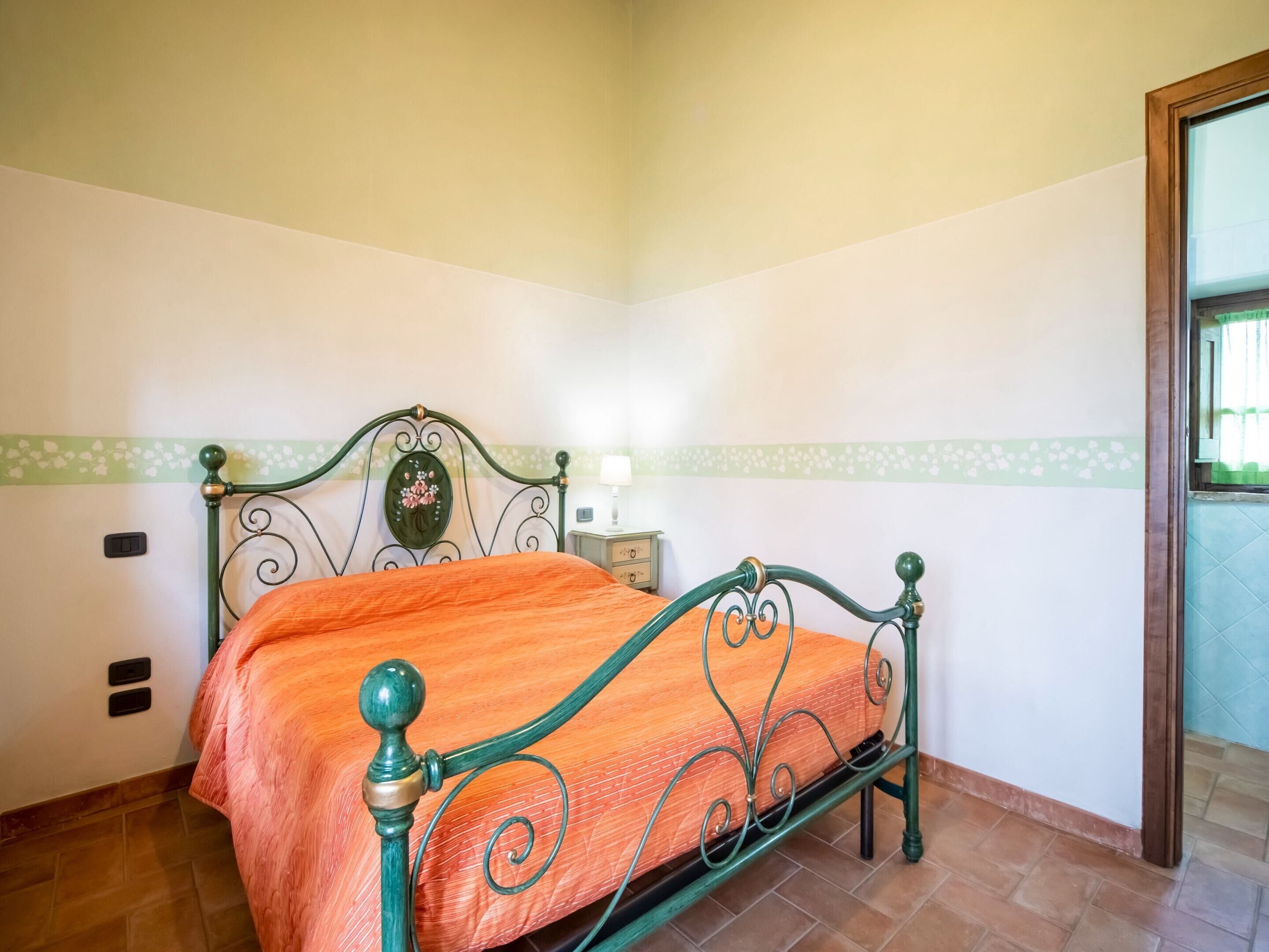 A bedroom with a bed, a nightstand, a wall-mounted light, and a window.