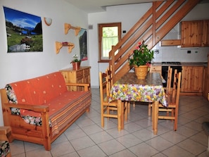 A cozy living room with a sofa, a dining table with chairs, a kitchen area, and a staircase.