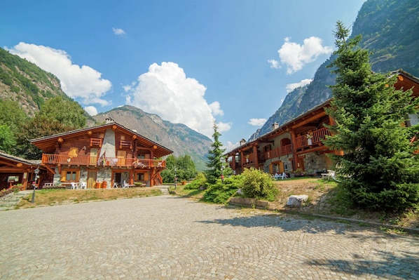 A wooden lodge with a stone facade, a stone courtyard, and mountainous backdrop.