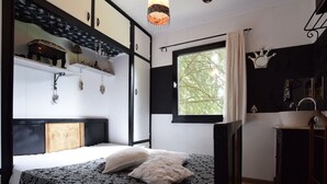 A bedroom with a bed, a window with a view of trees, a bathroom with a sink, and a decorative crown on the wall.