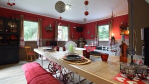 A kitchen with a long wooden table, red chairs, and a red bench. There are hanging decorations and a window with curtains.