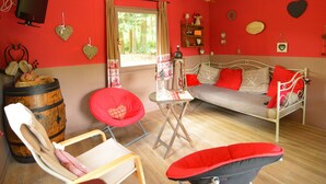 A room with a red and white color scheme, a bed with red and white bedding, a red chair, a wooden barrel, and a television on the wall.