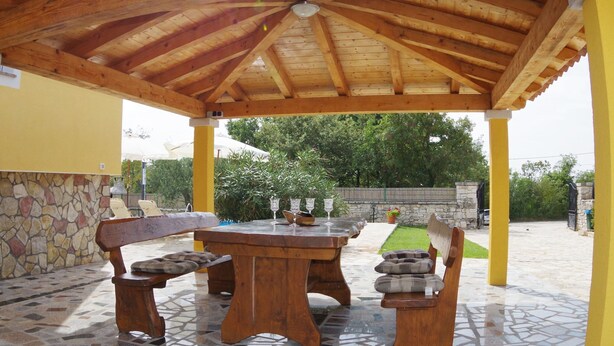 Une terrasse extérieure avec une table et des bancs en bois, entourée d’un mur en pierre et dotée d’un sol carrelé.