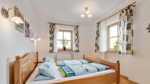 A bedroom with a wooden bed, two windows with patterned curtains, a radiator, and wall-mounted lights. - Apartment With all Amenities, Garden and Sauna (Schoensee)