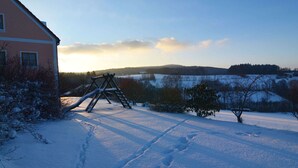 A snow-covered landscape with a wooden swing set and footprints in the snow. - Apartment With all Amenities, Garden and Sauna (Schoensee)