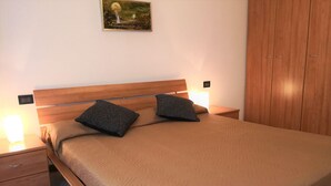 A neatly made bed with a wooden headboard, two pillows, and a bedside table with a lamp. - Holiday Home Lazise Near Lake and Gardaland (Lazise)