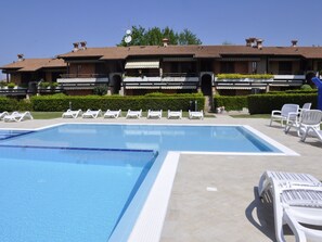 Ett poolområde med två pooler, vita solstolar och en byggnad med ett tak täckt av kakel i bakgrunden.