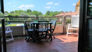 A patio with a table and chairs, a white chair, and a view of greenery and buildings in the distance. - Holiday Home Lazise Near Lake and Gardaland (Lazise)