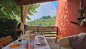 Un espace de restauration en plein air avec une table dressée pour deux personnes, un banc en bois et une vue sur un paysage luxuriant.