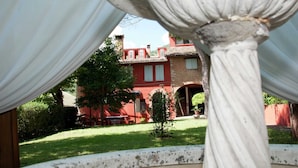 Une vue d’un bâtiment en briques rouges, avec un jardin et une colonne blanche au premier plan.