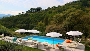 Une piscine entourée d’une végétation luxuriante et de collines, avec des chaises longues et des parasols à proximité.
