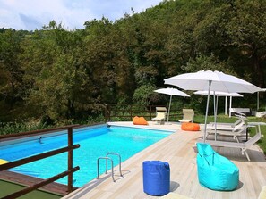 Ein Schwimmbad mit Holzterrasse, Liegestühlen und Sonnenschirmen.