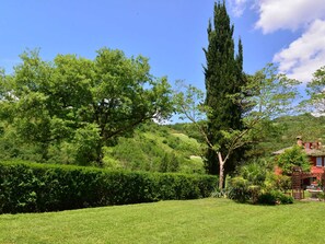 A lush green landscape with a variety of trees, a well-maintained lawn, and a distant view of a hill with a building. - Belvilla by OYO Casa Oro (Fabriano)
