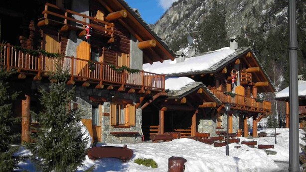 Un chalet en bois doté d’un balcon, de murs en pierre et d’un toit recouvert de neige.