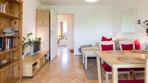 A cozy living room with a wooden bookshelf, a TV, a dining table with chairs, and a sofa with cushions. - Apartment Krakow Near Wawel Castle (Kraków)