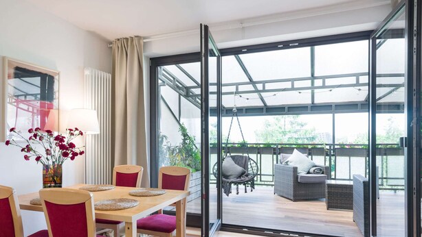 A modern room with a dining table, chairs, and a hanging chair. It features large glass doors leading to an outdoor patio with a sofa and a hanging chair. - Apartment Krakow Near Wawel Castle (Kraków)