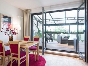 A modern room with a dining table, chairs, and a hanging chair. It features large glass doors leading to an outdoor patio with a sofa and a hanging chair.