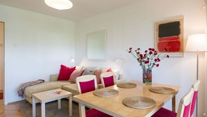 A modern living room with a sofa, a dining table with chairs, a vase with flowers, and a lamp. - Apartment Krakow Near Wawel Castle (Kraków)