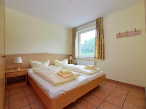 A double bed with two pillows, a bedside table with a lamp, a window with curtains, and a wall-mounted hook. - Ferienhaus in Willingen mit Skilift in der Nahe (Willingen)