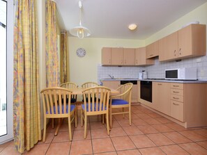 A kitchen with wooden cabinets, a microwave, and a dining area with chairs and a table.