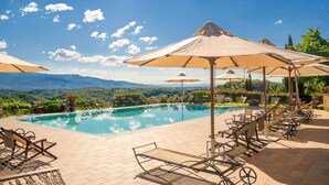 Un área de piscina con sillones y sombrillas, rodeada de montañas.