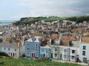 A coastal town with a mix of residential buildings, some with bay windows and a prominent hill in the background.