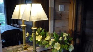 A table lamp with a vintage design, a mirror reflecting a dining area, and a decorative floral arrangement on a wooden surface. - Lodge in Appledore Near Camber Sands Beach (Romney Marsh)