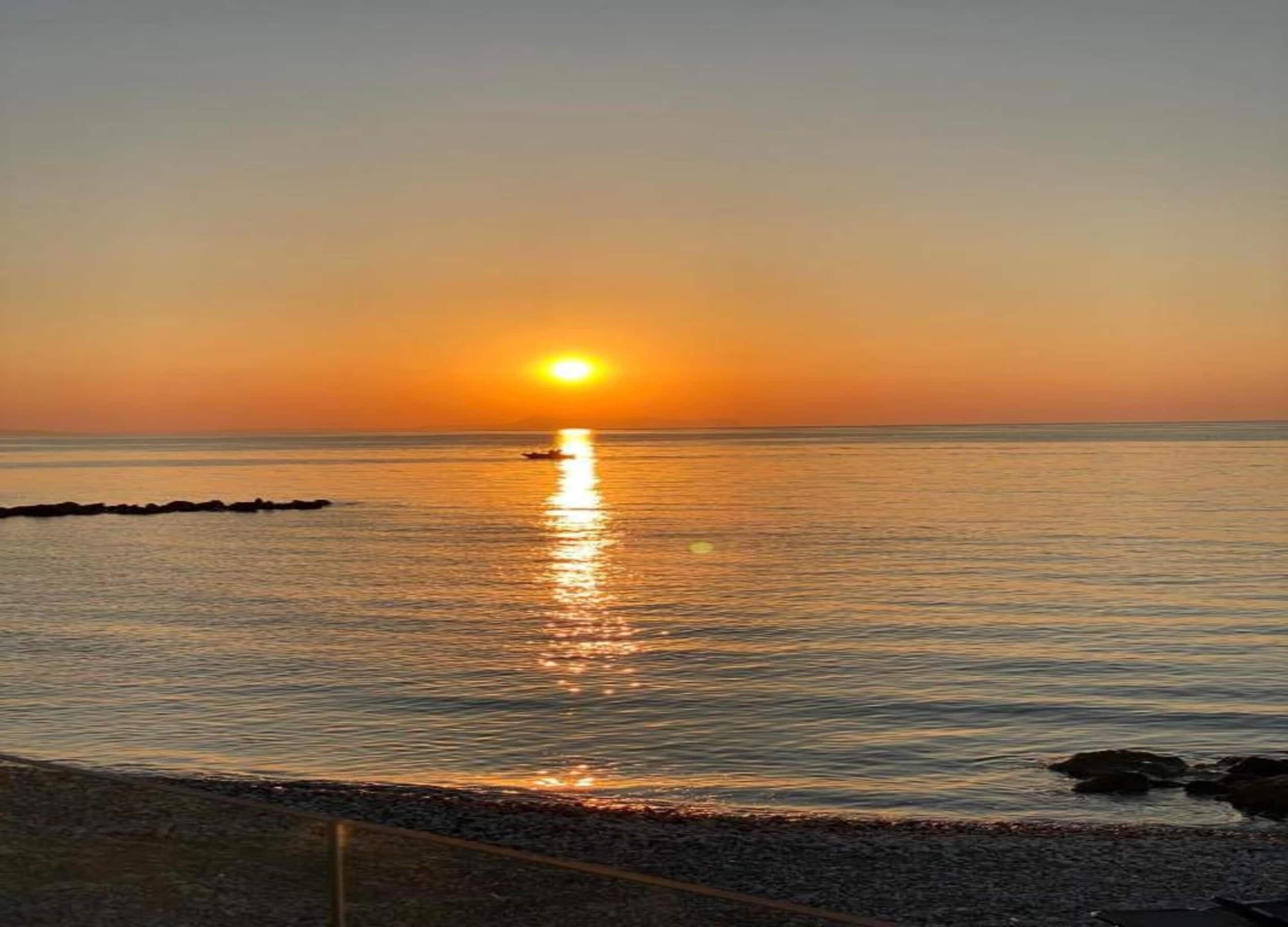 A sunset over a calm sea with a rocky shoreline.